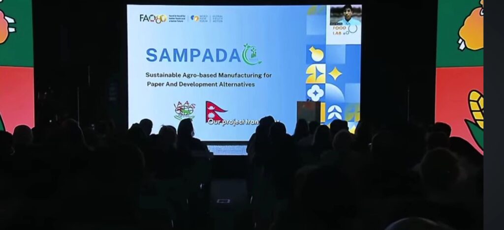 A compilation of four images documenting a global agricultural innovation event. The first image shows a large screen in a dark auditorium with the project title: "SAMPADA: Sustainable Agro-based Manufacturing for Paper And Development Alternatives," featuring the Nepali flag and the presenter in a corner window. The second image is a certificate for the "Youth Food Lab Award (EUR 1000)" won by SAMPADA. The third image is a certificate for the "Youth Food Lab x Learning Factory Award" won by SAMPADA, highlighting support from Penn State and The Learning Factory.